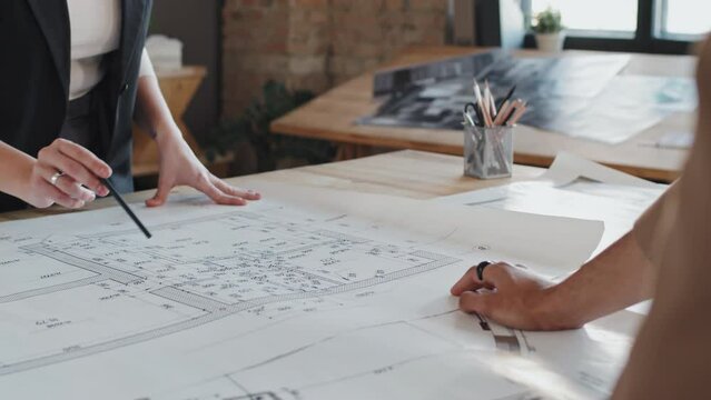 Midsection of two cropped architects discussing floor plan at table in office at daytime