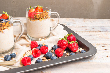 Granola with nuts, yogurt and red fruits berries in a jar. Breakfast parfait with muesli, yoghurt, red fruits berries and honey, white kitchen background.