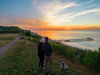 Pärchen mit Hund beobachten den Sonnenaufgang an der Ostsee