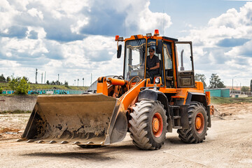 A large front loader transports crushed stone or gravel in a bucket at a construction site or concrete plant. Transportation of bulk materials. Construction equipment. Bulk cargo transportation.