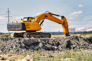 A powerful caterpillar excavator digs the ground against the blue sky. Earthworks with heavy equipment at the construction site.