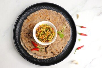 Super spicy green and red bird eye chili chutney using lal and hari mirch, garlic cloves, and coriander. served in a white bowl. Also known as Thecha in Marathi served with Raagi roti. copy space