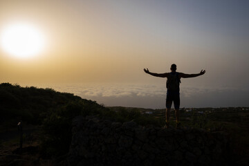Fototapeta na wymiar Siluette of tall male hiker on mountain above clouds in sunrise on El Hierro island in summer