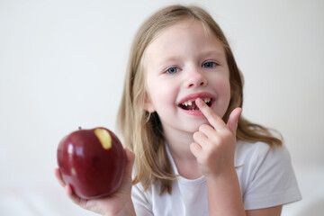 Portrait of smiling cute girl without teeth with red bitten apple in hand