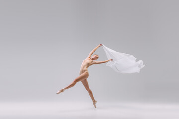 Portrait of young tender ballerina dancing with fabric isolated over grey studio background....