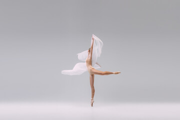 Fototapeta na wymiar Portrait of young ballerina dancing with transparent fabric isolated over grey studio background. Standing on tiptoe on pointe