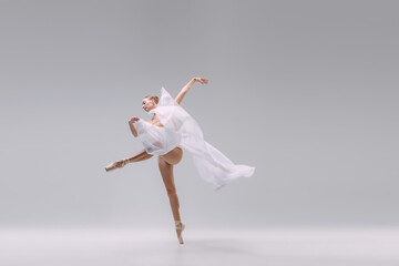 Portrait of young gracefull ballerina dancing with transparent white fabric isolated over grey studio background