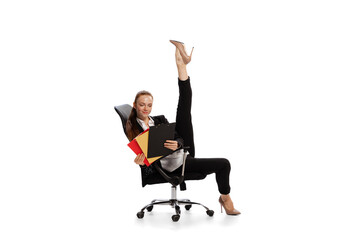 Smiling young office worker in business style clothes with folder sitting on chair, reading papers and making twine isolated over white background.