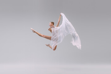Portrait of young graceful ballerina dancing with transparent fabric isolated over grey studio background. Weightless jump - obrazy, fototapety, plakaty