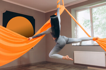 beautiful young girl doing aerobic exercises in fly yoga on canvases near windows in gym