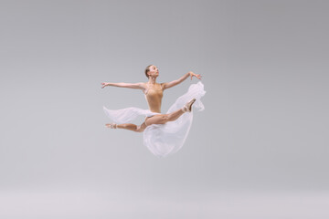 Portrait of young ballerina dancing with light transparent fabric isolated over grey studio background. Flying like a bird. Freedom