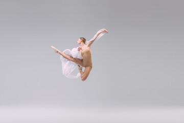 Portrait of young ballerina dancing with fabric isolated over grey studio background. Looks...