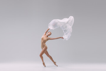 Portrait of young ballerina dancing in beige bodysuit with transparent fabric isolated over grey studio background. Tiptoe movements - obrazy, fototapety, plakaty