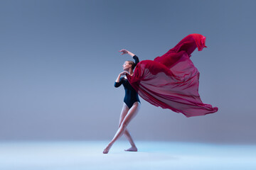 Portrait of young ballerina dancing in black bodysuit with deep red fabric isolated over blue grey...