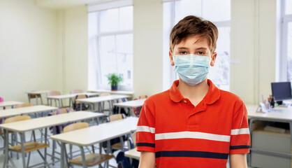 school, education and pandemic concept - student boy in protective medical mask over empty classroom background