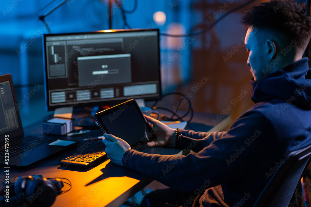 Poster cybercrime, hacking and technology concept - close up of male hacker in dark room with tablet pc usi