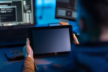 cybercrime, hacking and technology concept - close up of male hacker in dark room with tablet pc...