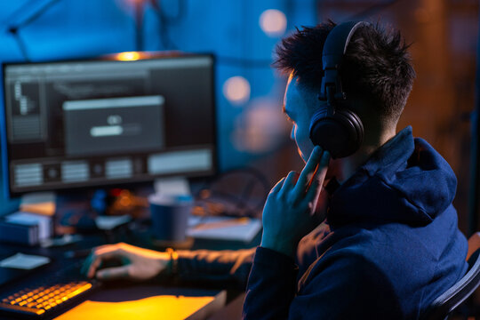 cybercrime, hacking and technology concept - close up of male hacker in dark room writing code or using computer virus program for cyber attack