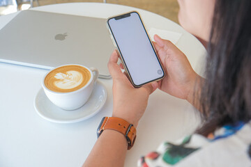 Asian women use smartphone in cafe drinking hot latte art coffee