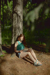 Redhead beautiful european woman sitting in the forest and reading a book.