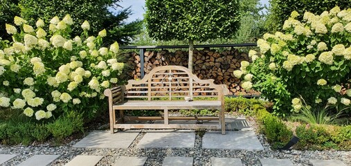 Lawka w ogrodzie w stylu angielskim z drewna tekowego wśród hortensji