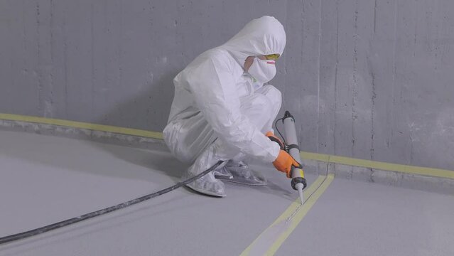 The builder covers the joint seam with sealant. Construction worker grouting seams in concrete floor