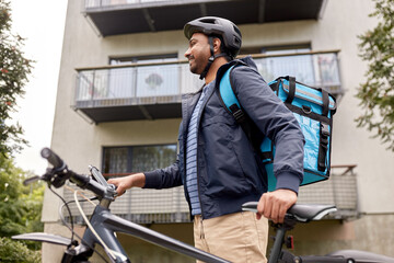 food shipping, profession and people concept - happy smiling indian delivery man with thermal insulated bag and bicycle on city street