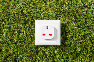 electricity, energy and power consumption concept - close up of socket on green grass background