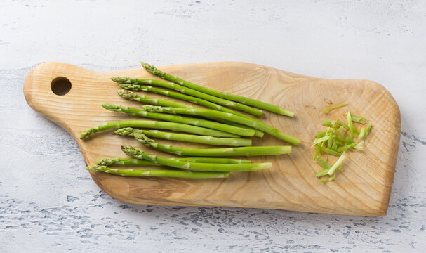 Wooden board of fresh asparagus with cut tough pieces on a light blue background, home cooking