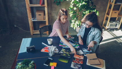High angle view of young female designers are placing photos on broad table to create perfect flat...