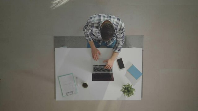 Man wearing headphones, working on laptop and having call. Top down shot of workplace. Home office workroom from height.