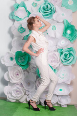 Young attractive girl with blond hair with trendy make-up and hairstyle in a white trendy jumpsuit with paper flowers decor