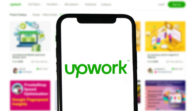 Upwork logo is displayed by a modern smartphone, in the background the website of the online platform for digital services, freelancing, self employment
