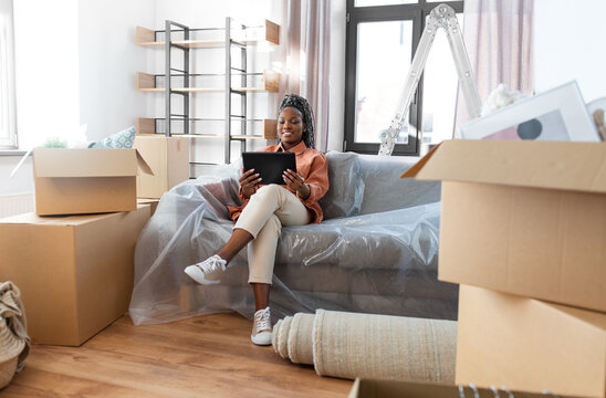 moving, people and real estate concept - happy smiling woman with tablet pc computer and boxes at new home