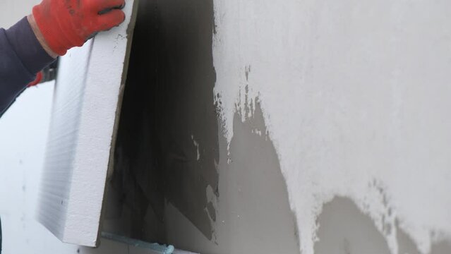 Construction worker installing styrofoam insulation sheets on house facade wall for thermal protection