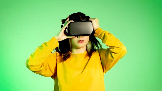 Metaverse concept, amazed young asian woman wearing black vr headset touching on the green neon screen background. 4K video asian girl futuristic style gamer.