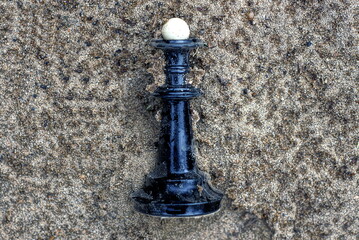 Obraz na płótnie Canvas one black dirty plastic chess piece queen lies on the gray sand in the street