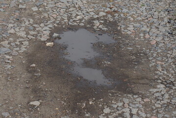 one big puddle with brown dirty water on the gray ground of a rural road in the street