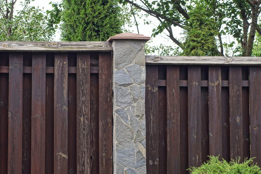 part on gray brown wall of a fence made of wooden boards and stones on the street