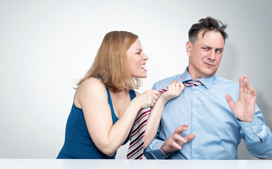 The woman in a rage grabbed the man by the tie and screams at him, the man covers himself with his hands and looks scared