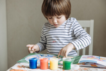 Finger painting. Portrait of cute little boy painting with fingers at home. Close-up of child's hand in colorful paints. Early education concept. Sensory play. Development of fine motor skills.