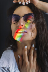 Closeup portrait of smiling woman with ray of rainbow light on her face. Rainbow optical flare from the window projected on her face. Beautiful young woman in colorful lights. art beauty portrait