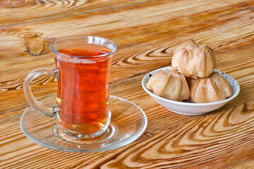 Traditional turkish glass cup of black tea with sweet profiteroles on wooden table.