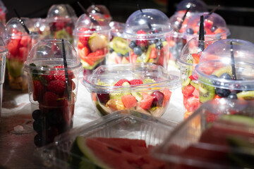 Delicious, colorful and fresh fruit pieces salad in plastic glasses placed on table. Blurred background.