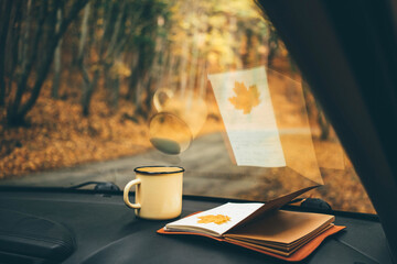 Yellow maple leaves in paper diary lies in car against rural road in picturesque autumn forest closeup.