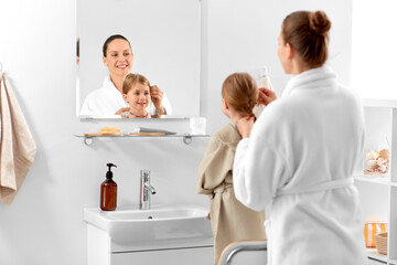 beauty, family and people concept - happy smiling mother and daughter looking to mirror and braiding hair in bathroom