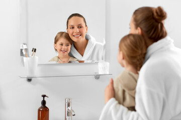beauty, hygiene, morning and people concept - happy smiling mother and daughter looking to mirror...