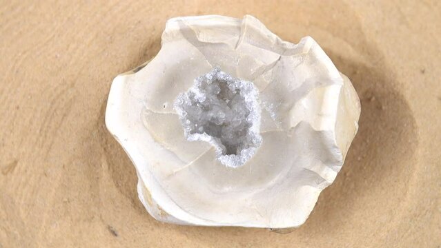 Sample of a geode rock crystal, of white color rotates on a sand background 