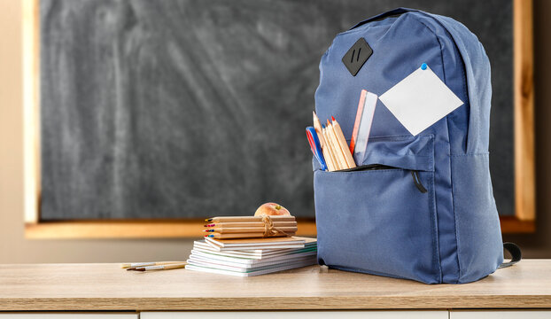 A school backpack on a wooden table with scattered supplies and a free space