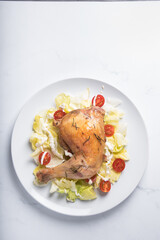 Baked chicken leg with lettuce leaves and cherry tomatoes on a white plate on a marble background